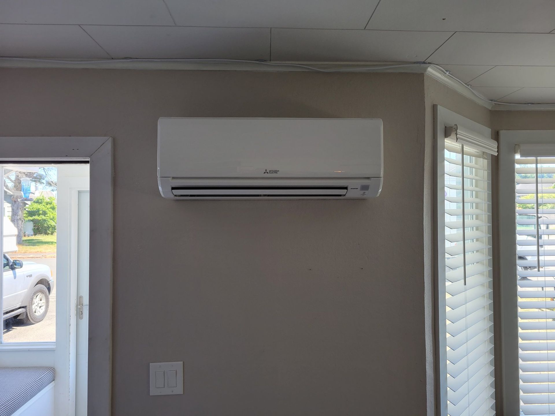 White wall-mounted air conditioning unit on a beige wall in a room.