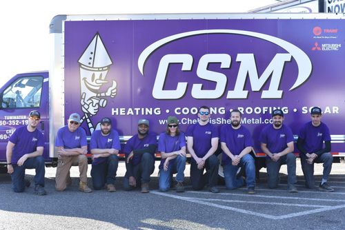 A group of people in purple shirts kneel in front of a CSM truck.