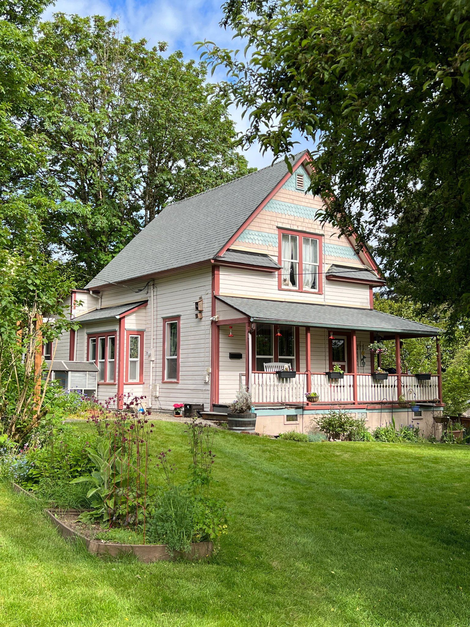 House with pink trim and porch, set in a green yard with trees under a blue sky.