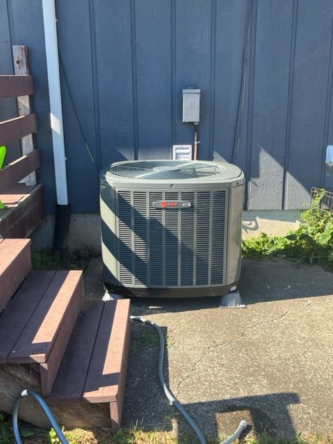 HVAC unit next to a building with a blue exterior. Concrete slab, stairs, and hose are visible.