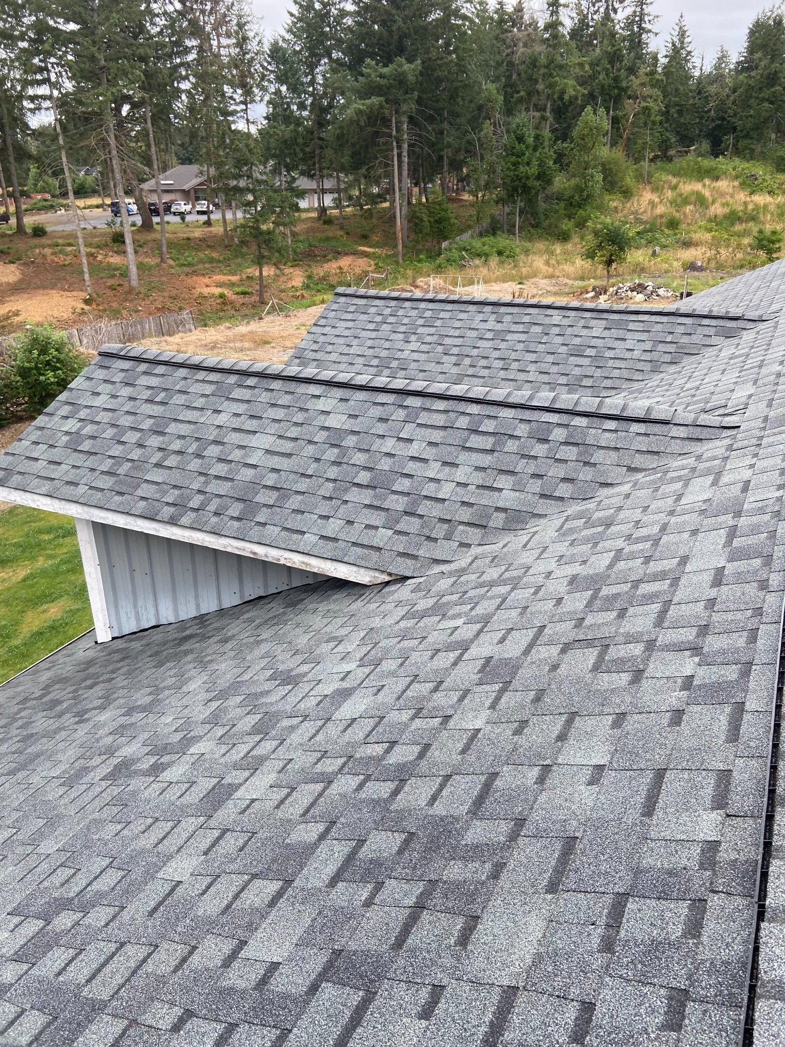 Gray asphalt shingle roof on a house, with a grassy area and trees in the background.
