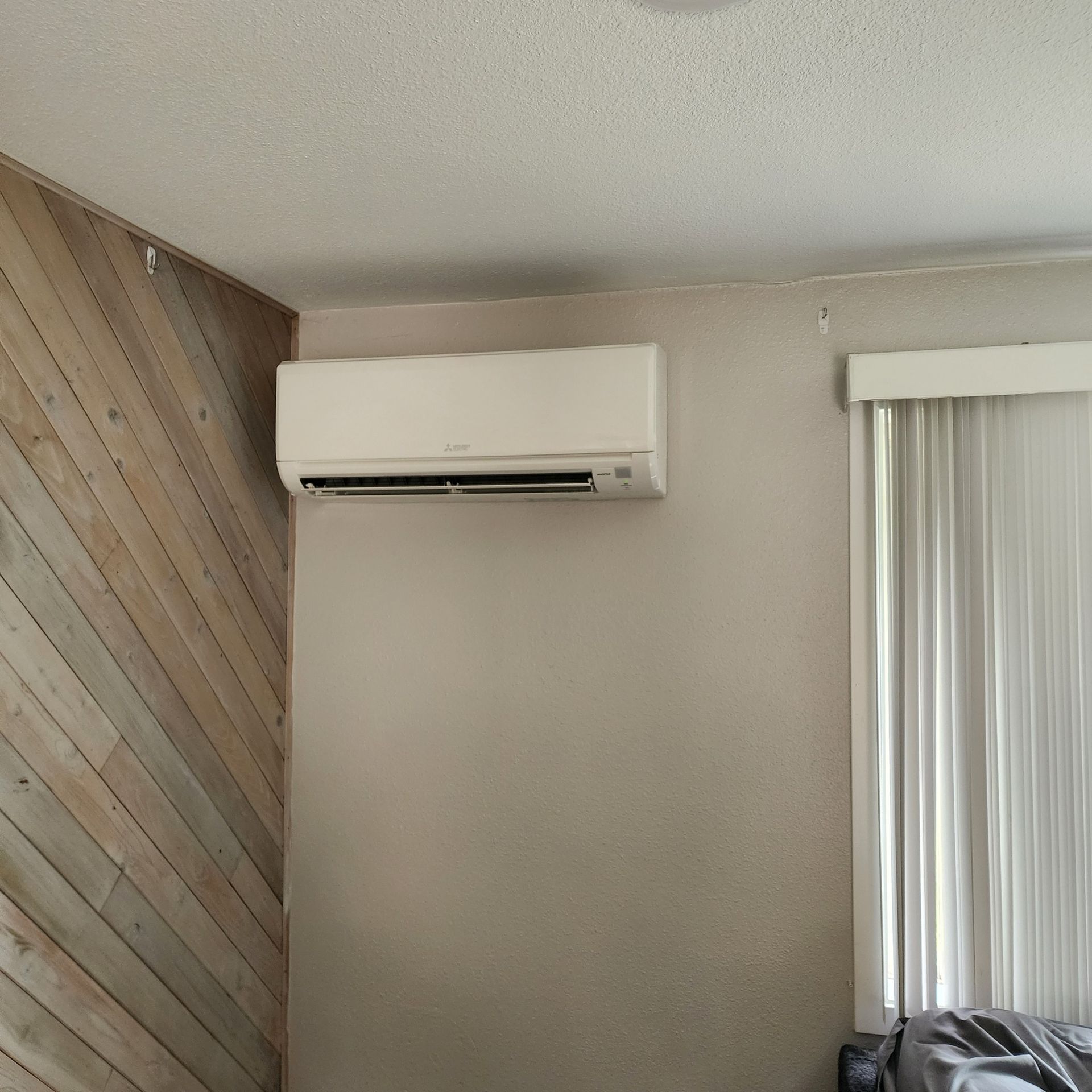 White air conditioning unit mounted on a light gray wall next to a window.