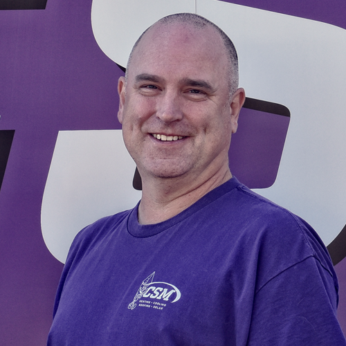 Man in purple shirt smiling in front of a purple and white background.