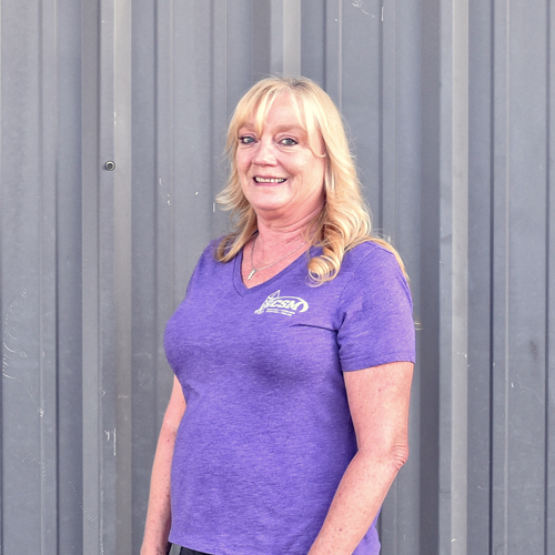 Woman in purple shirt smiles in front of a gray metal wall.