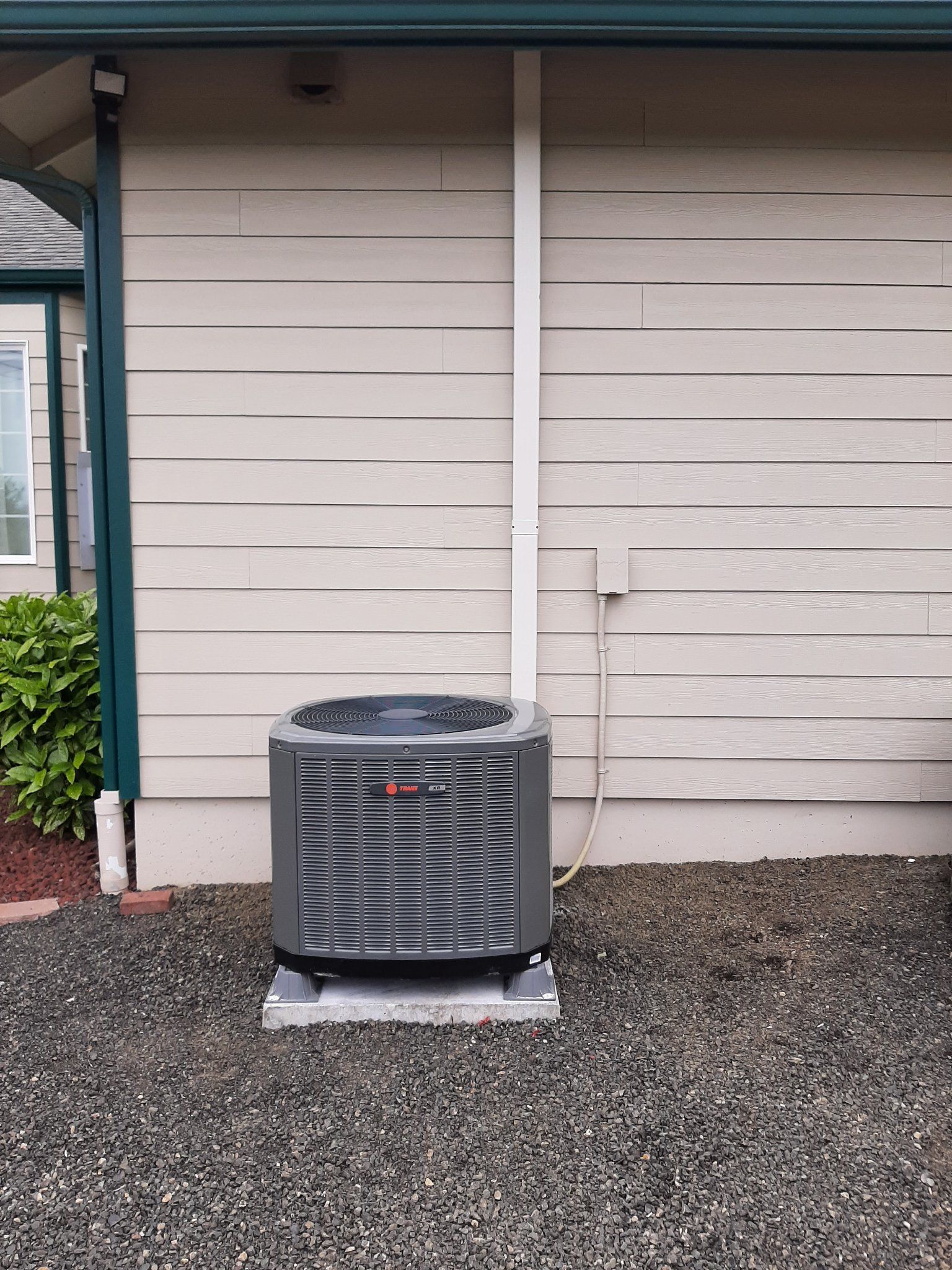 Air conditioning unit on a gravel bed next to a beige-sided house; white conduit and outlet.