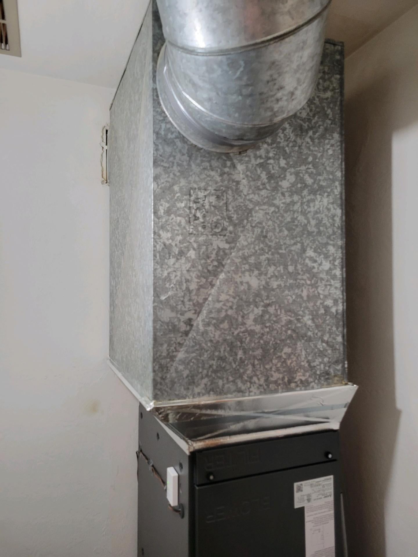 HVAC system with metal ductwork and furnace in a white-walled room.