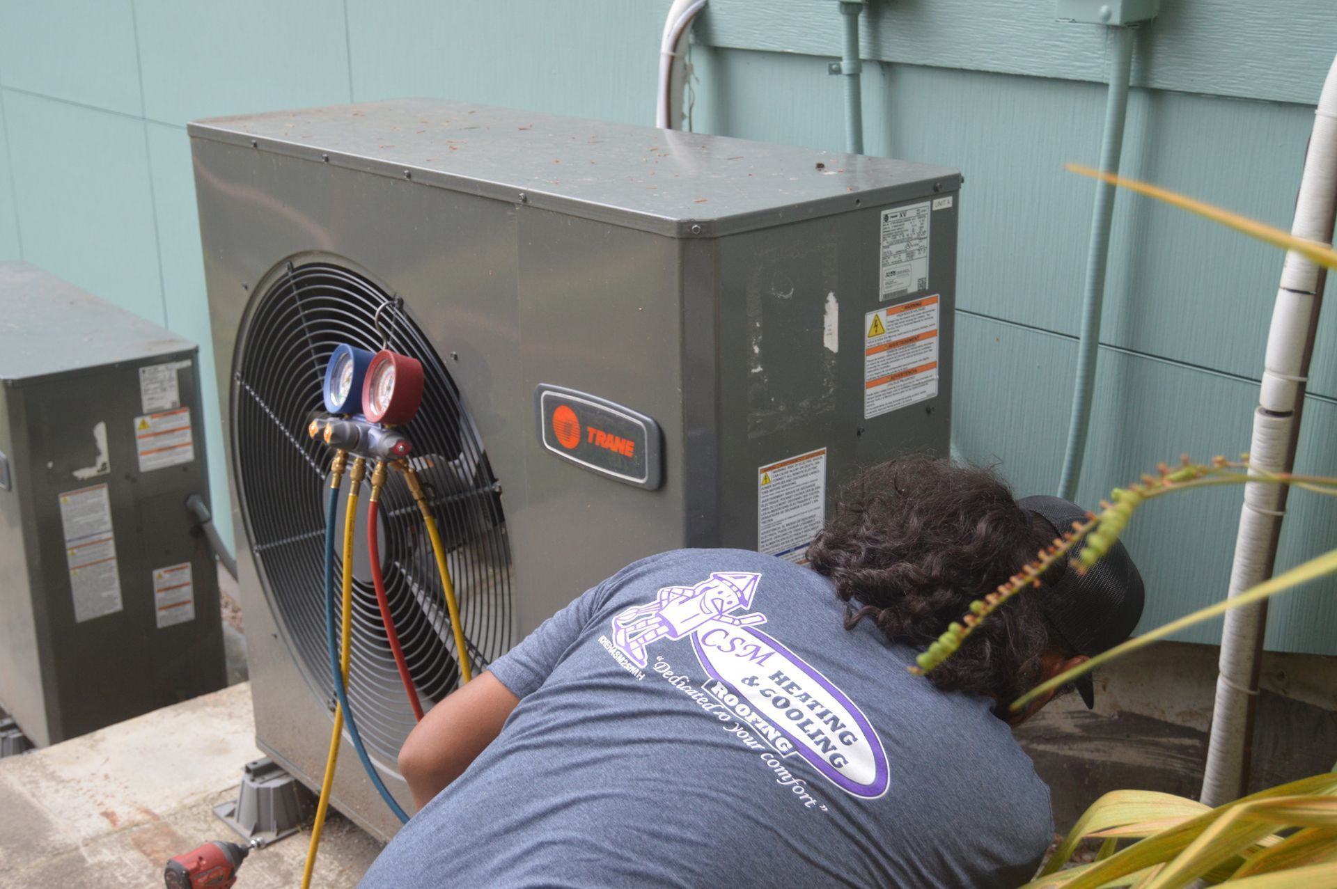 HVAC technician working on an air conditioning unit outside, gauges attached.