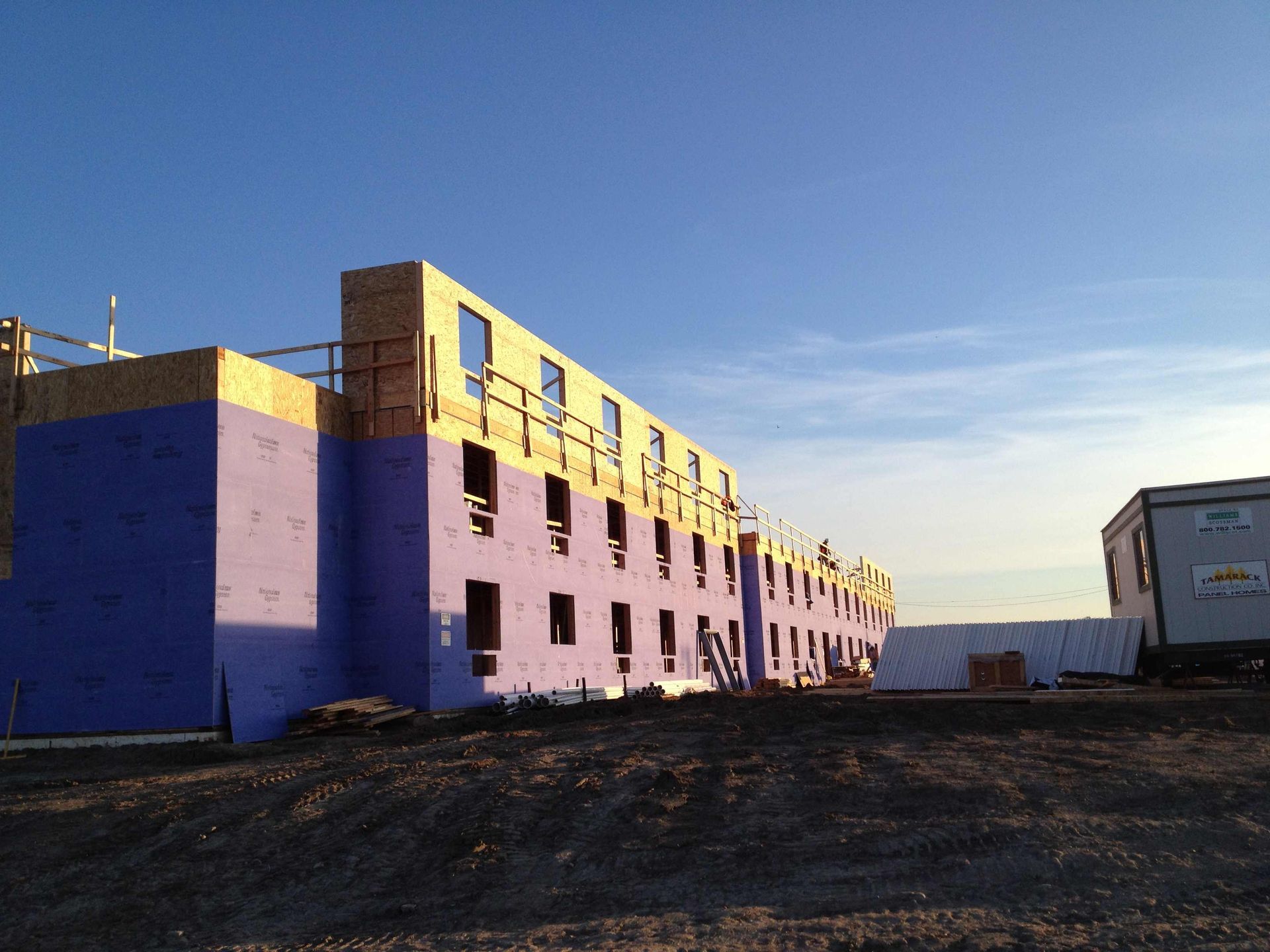 Purple building under construction on a dirt lot at sunset, with blue sky and a white trailer nearby