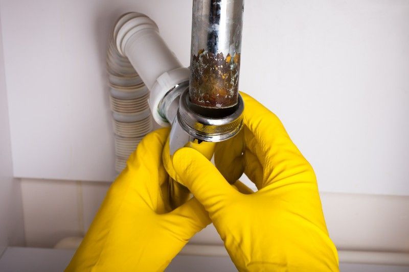 A person wearing yellow gloves is fixing a sink pipe.
