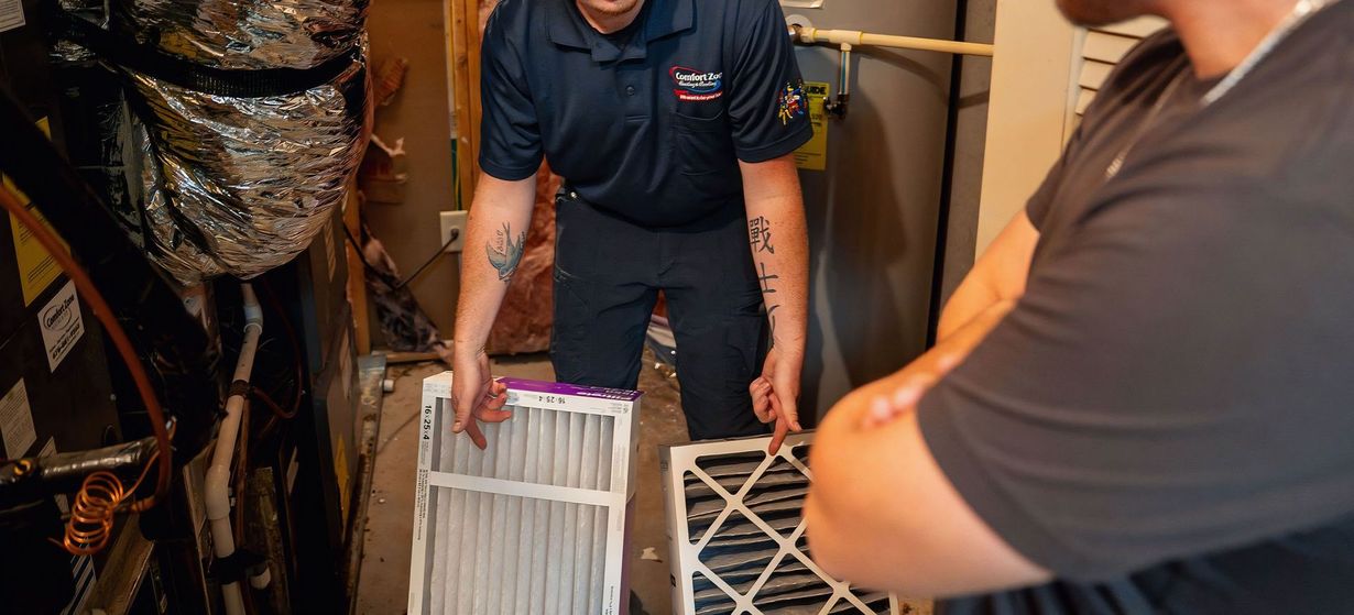 Two workers carrying air filters through a narrow utility space.
