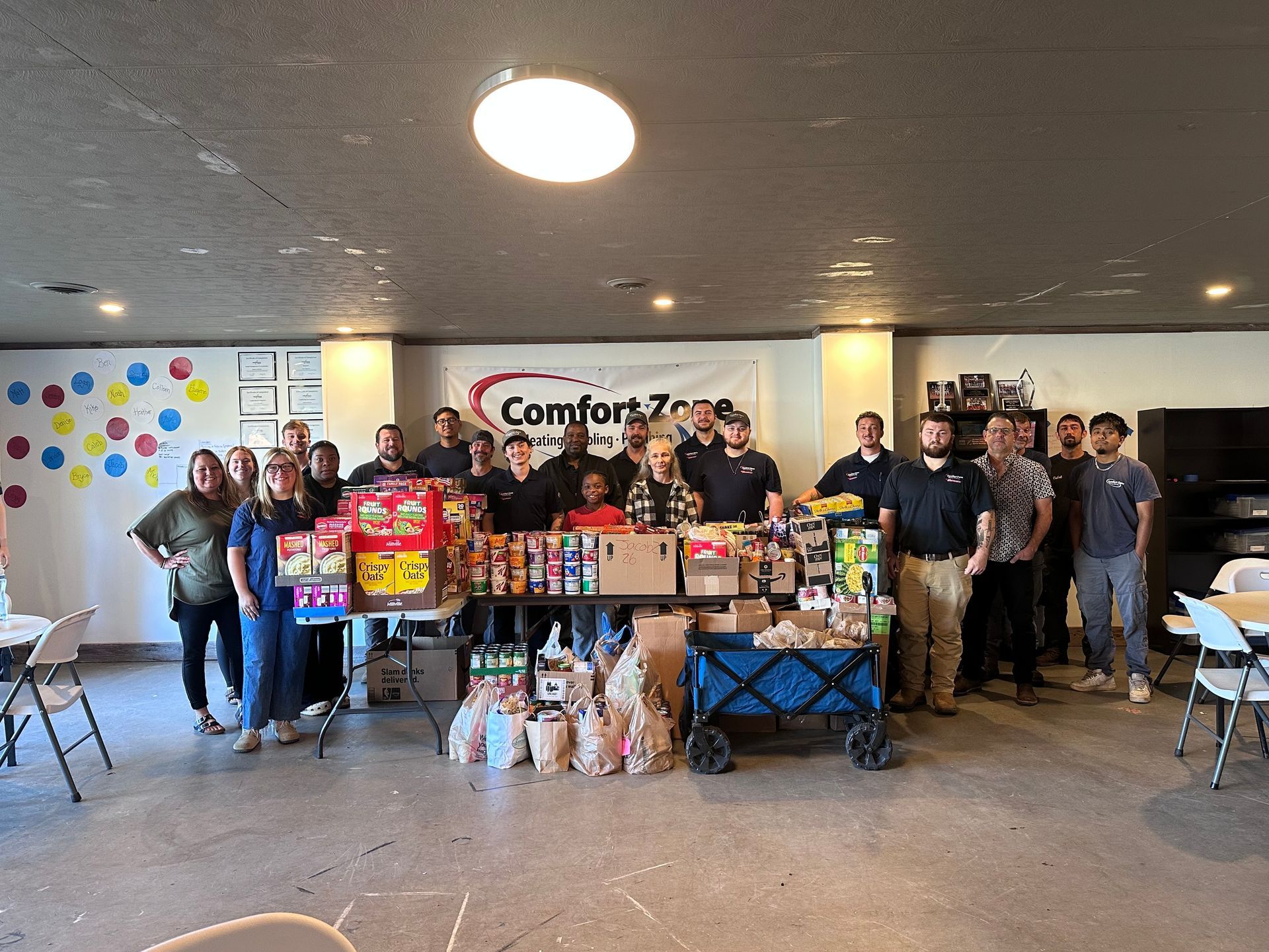 Group of volunteers posing behind a large food donation display in a community hall with a “Comfort Zone” sign.