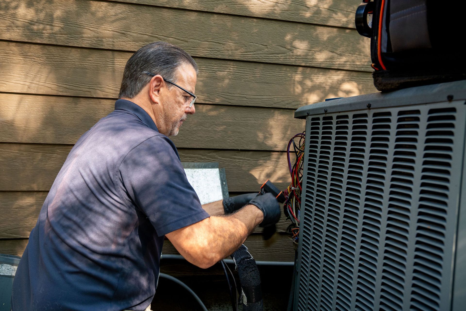Technician servicing an outdoor air conditioner unit beside a house