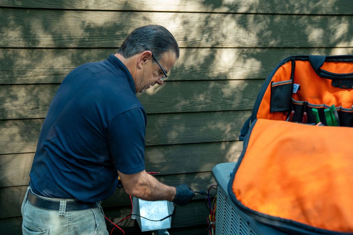 Technician servicing an outdoor air conditioner unit with tools and gauges attached.
