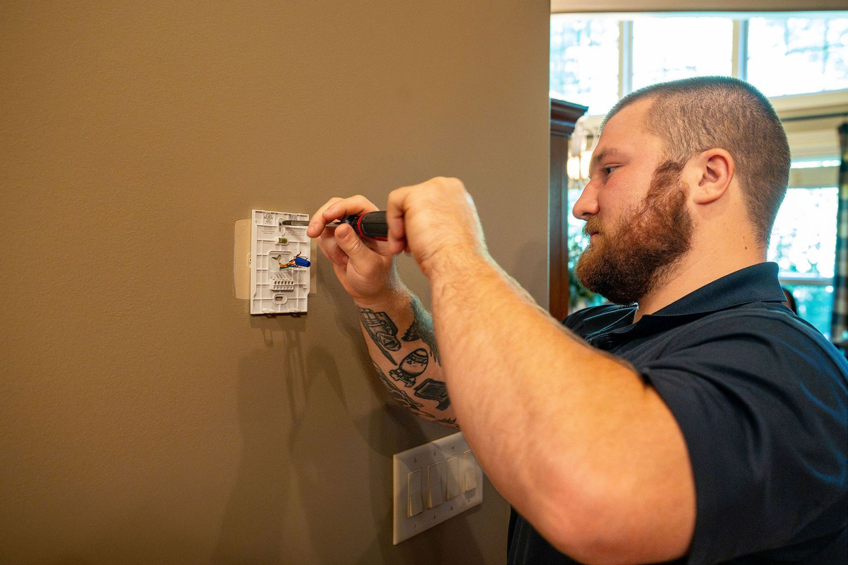 Man installing a wall switch with a screwdriver beside a beige wall and doorway
