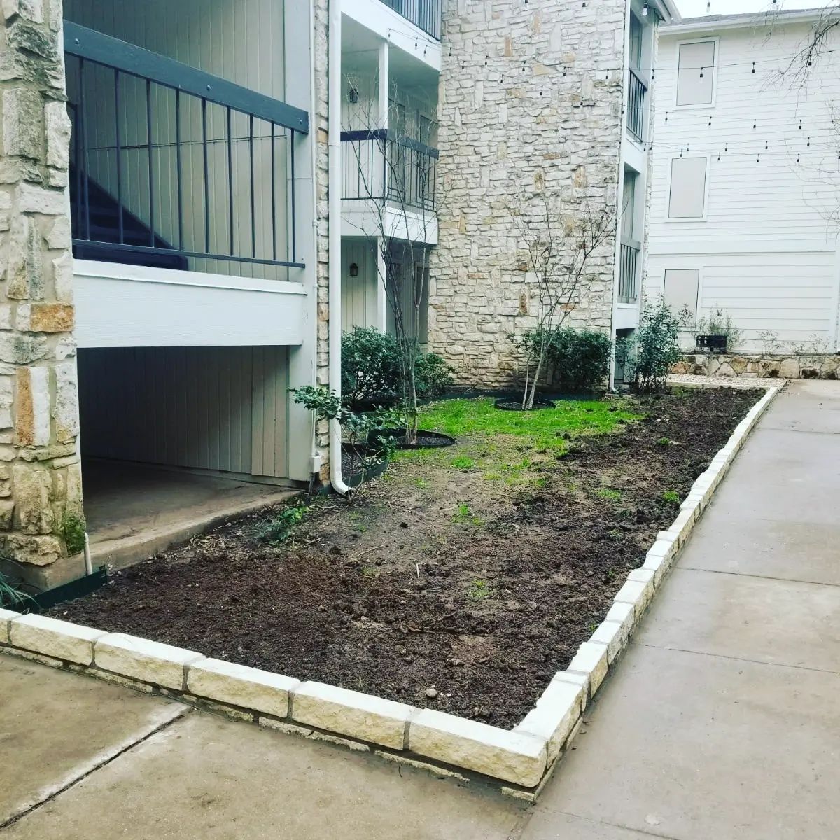 A concrete walkway leading to a building with a stone wall.