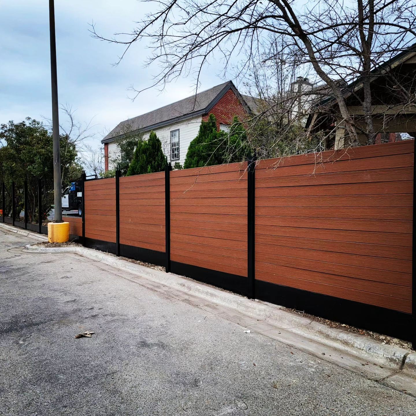 A wooden fence is along the side of a road in front of a house.