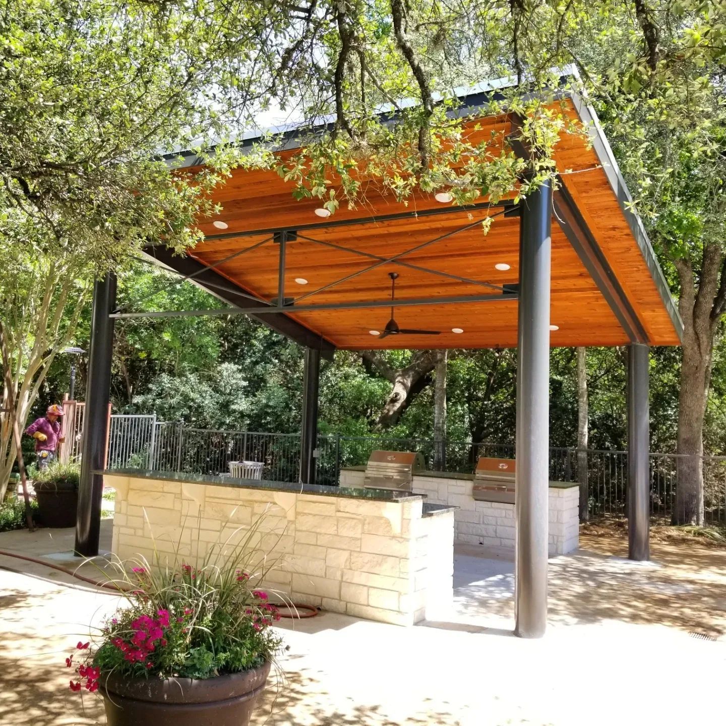 A wooden gazebo with a ceiling fan is surrounded by trees.