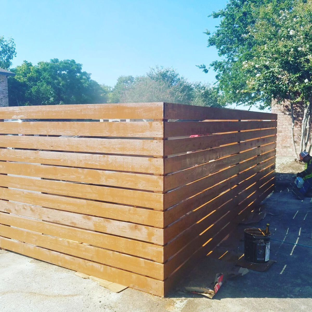 A wooden fence is being painted on a sunny day.
