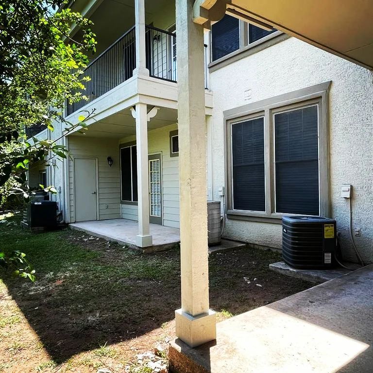 A white house with a black air conditioner in the backyard.