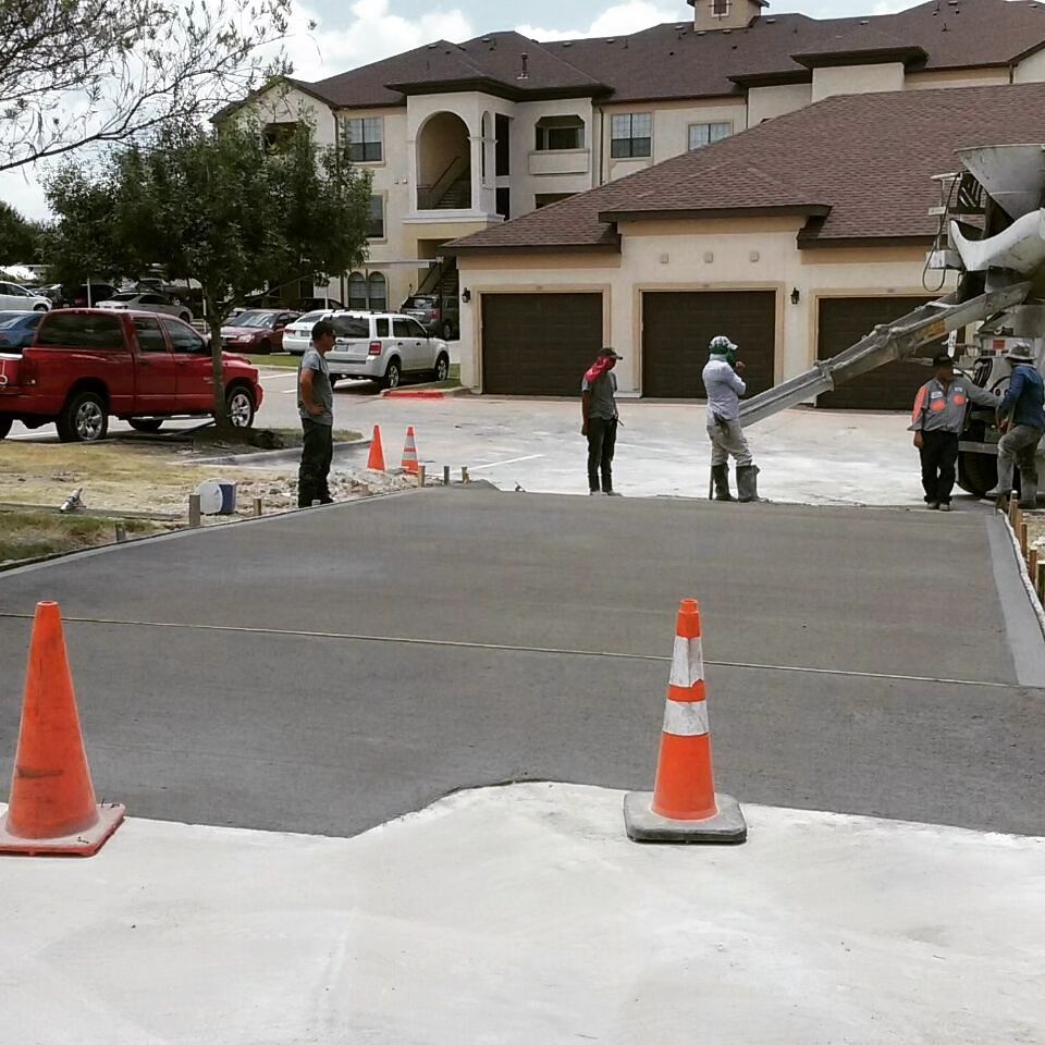 A group of construction workers are working on a driveway in front of a large house.