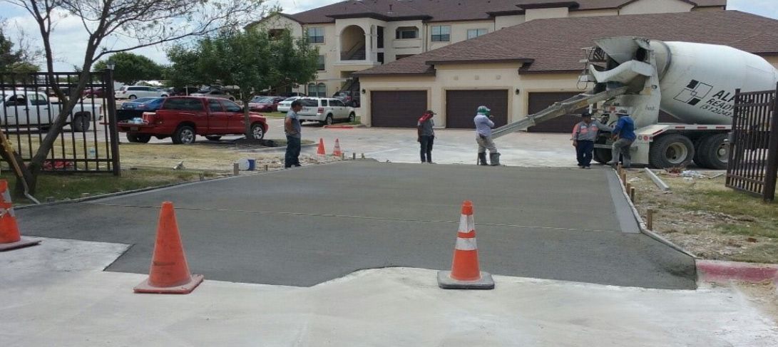 A concrete truck is pouring concrete into a driveway in front of a house.