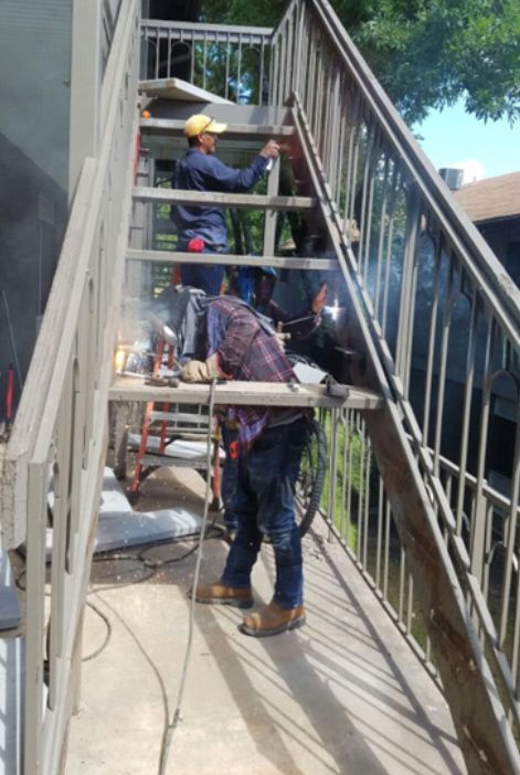 A man is welding a metal railing on a set of stairs.