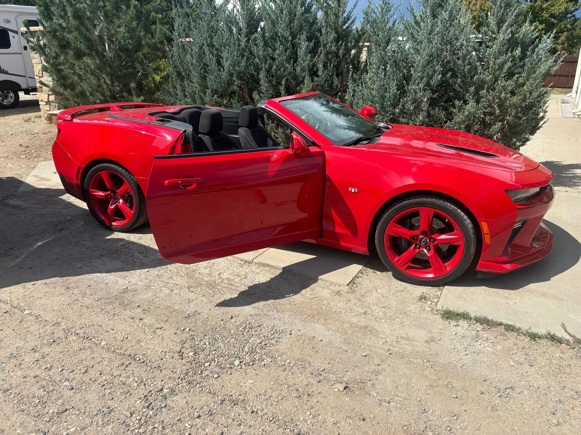 Red convertible car with matching rims, door open, parked on gravel.