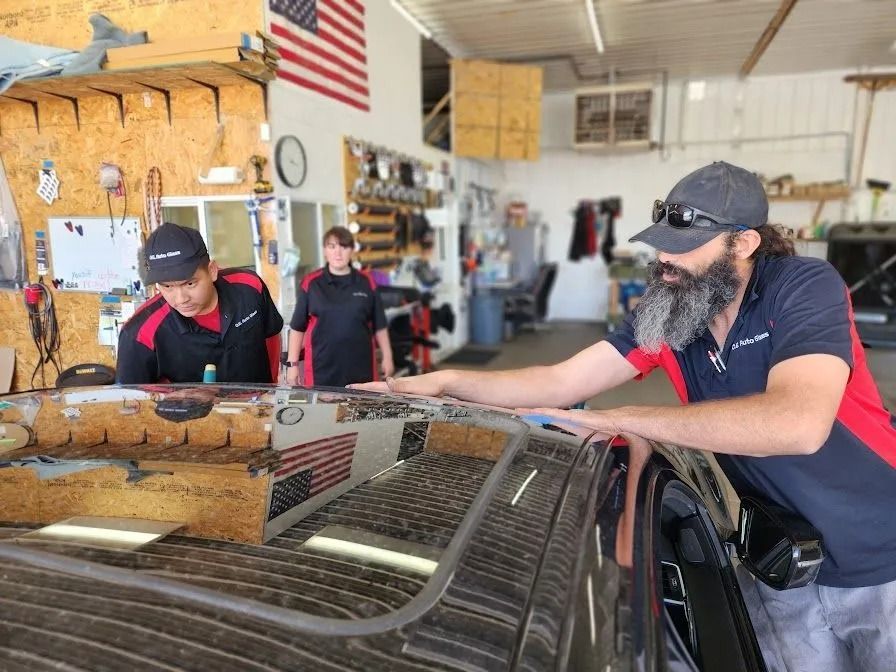Three people examining a car roof in a garage. One man points, two others watch. American flag visible.