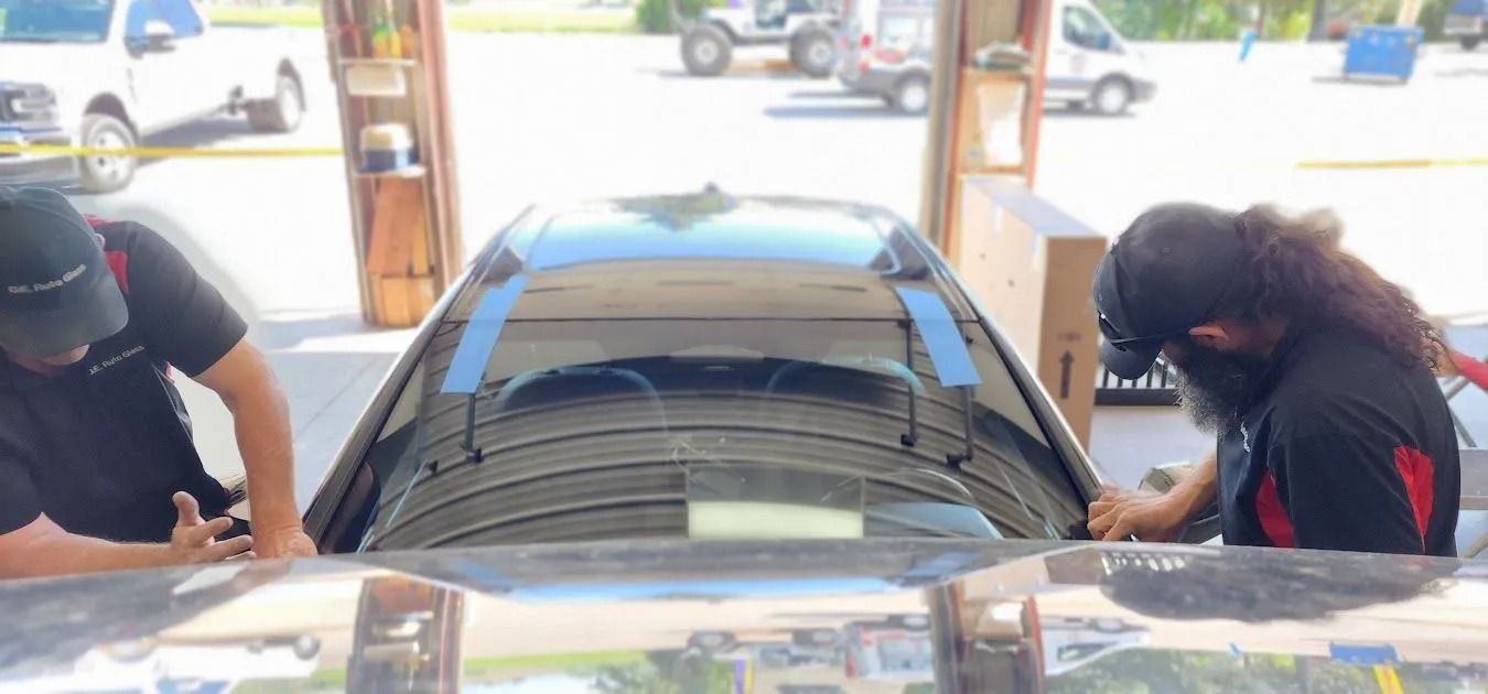 Two people installing a car window in a garage.