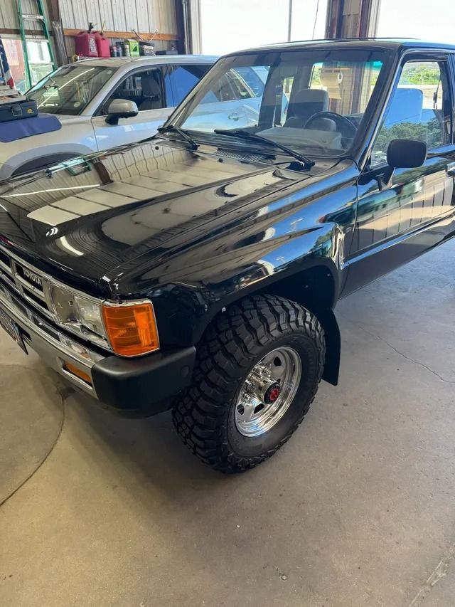 Black Toyota pickup truck with off-road tires, parked in a garage.