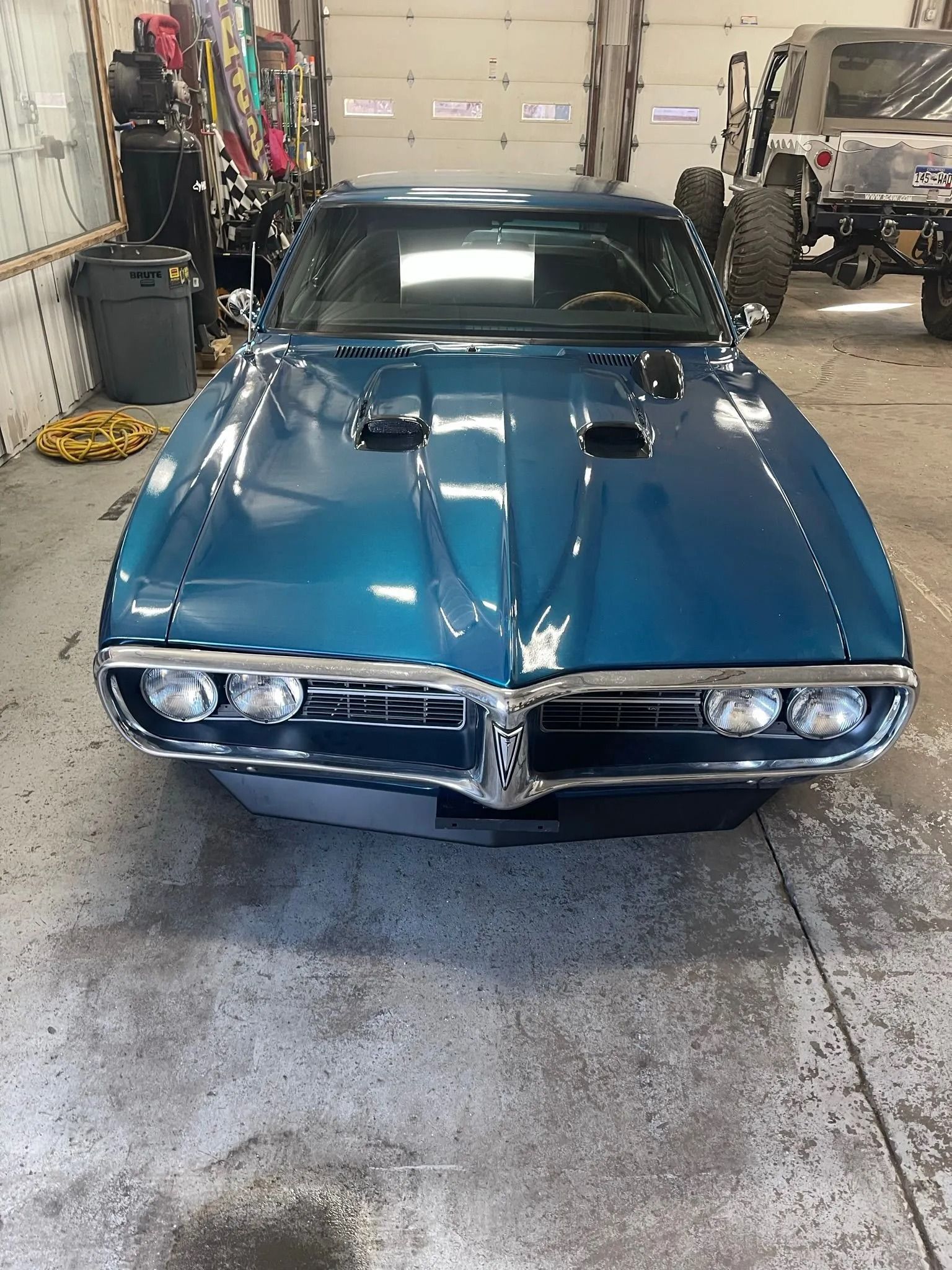 Teal 1968 Pontiac Firebird in a garage setting with a gray concrete floor.