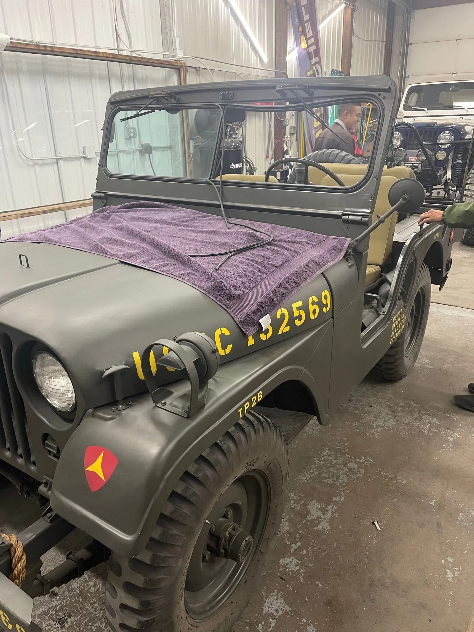 Green military Jeep with open top, parked indoors. Number 