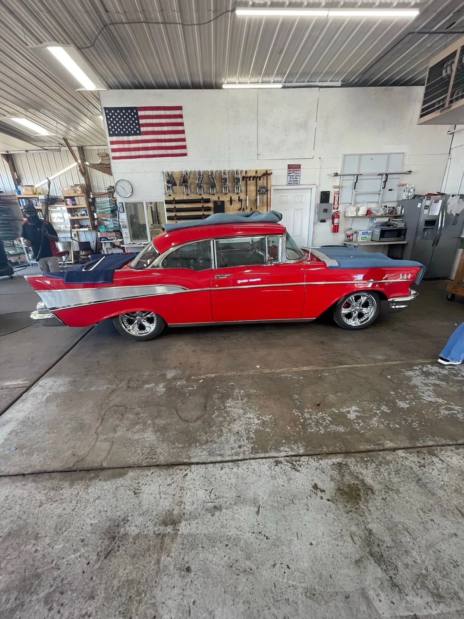 Red classic car with chrome wheels in a garage, American flag in background.