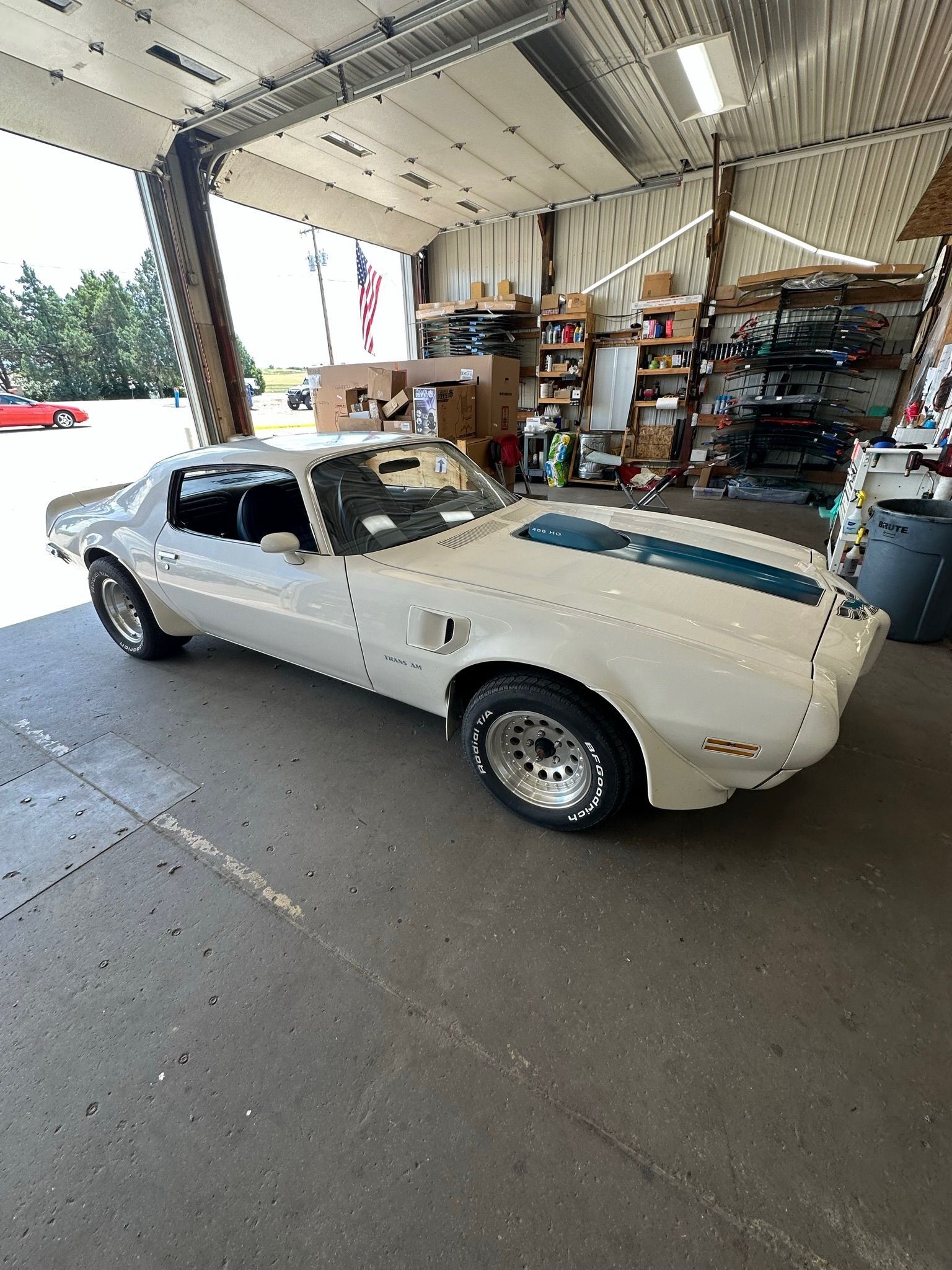 White Pontiac Firebird Trans Am with blue stripes inside a garage.