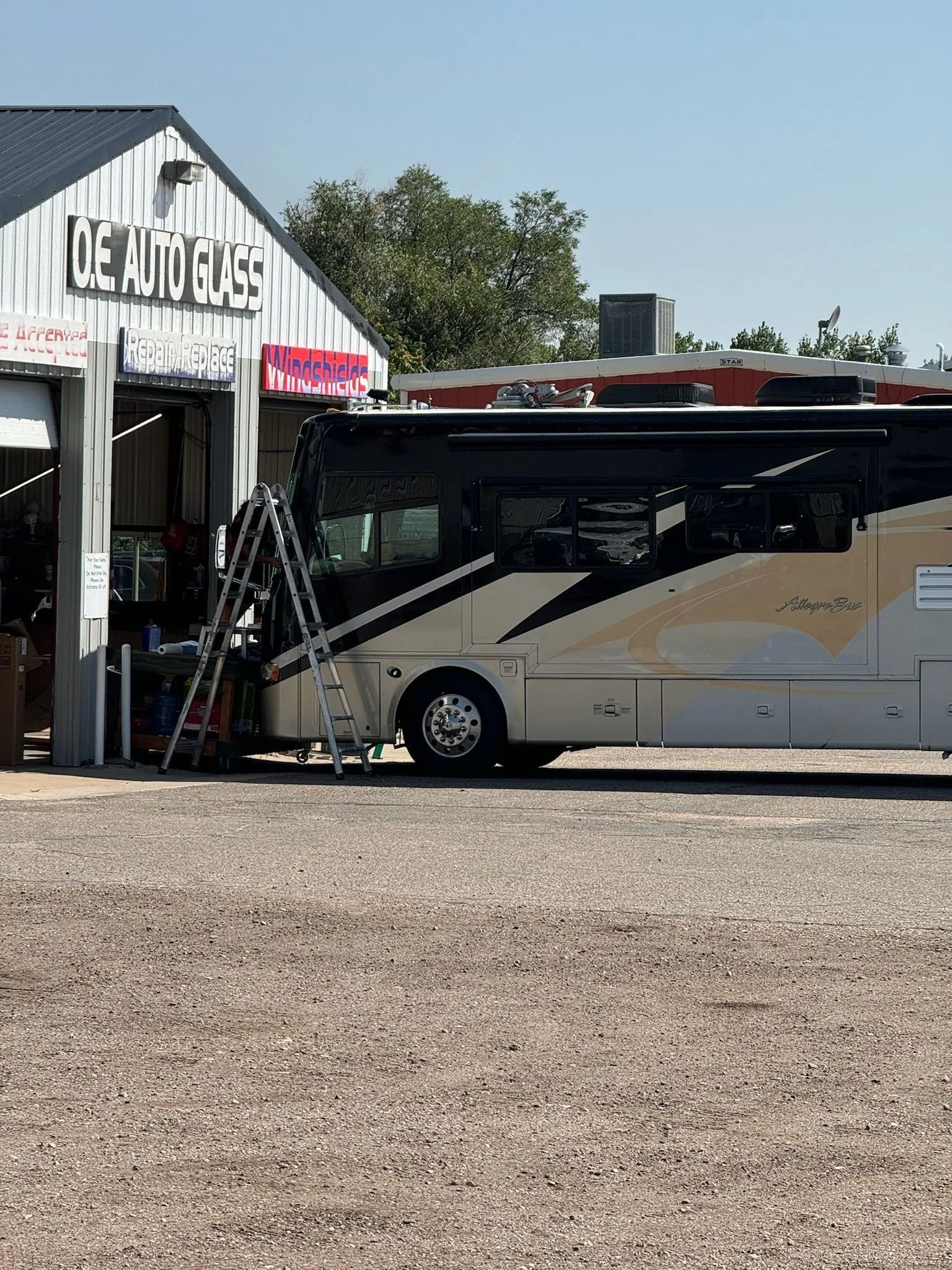 RV parked at an auto repair shop with a ladder propped against it.