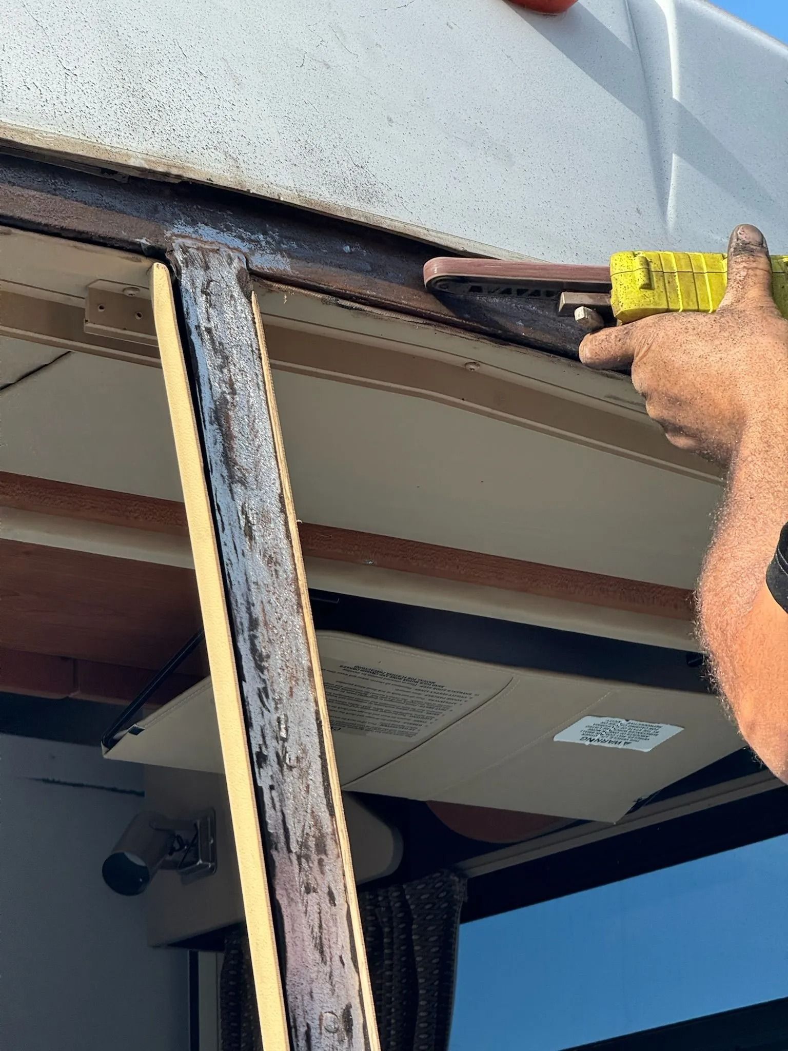 Person applying sealant to a boat's roof edge with a yellow caulking gun, outdoors.