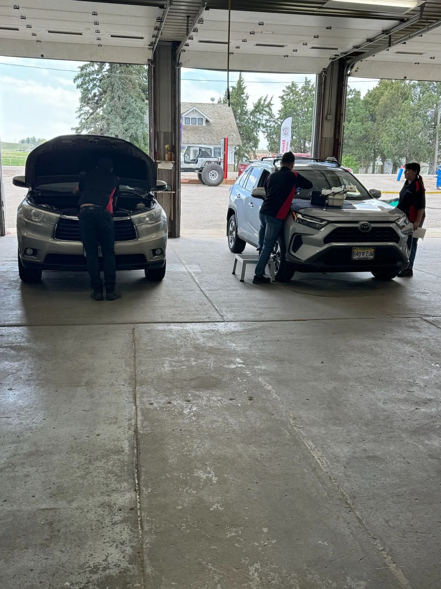 Two vehicles being worked on inside a garage. Mechanics are inspecting the vehicles.