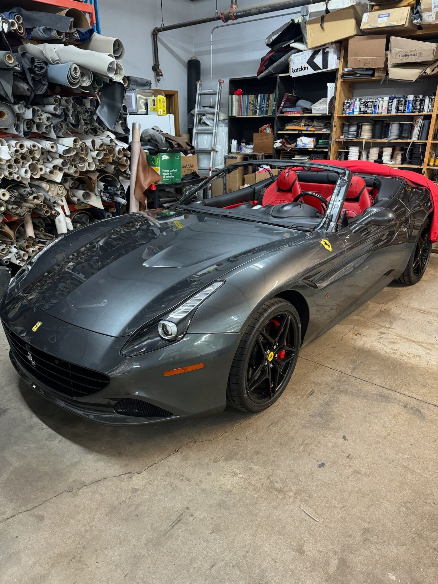 Gray Ferrari convertible with red interior, parked in a garage.