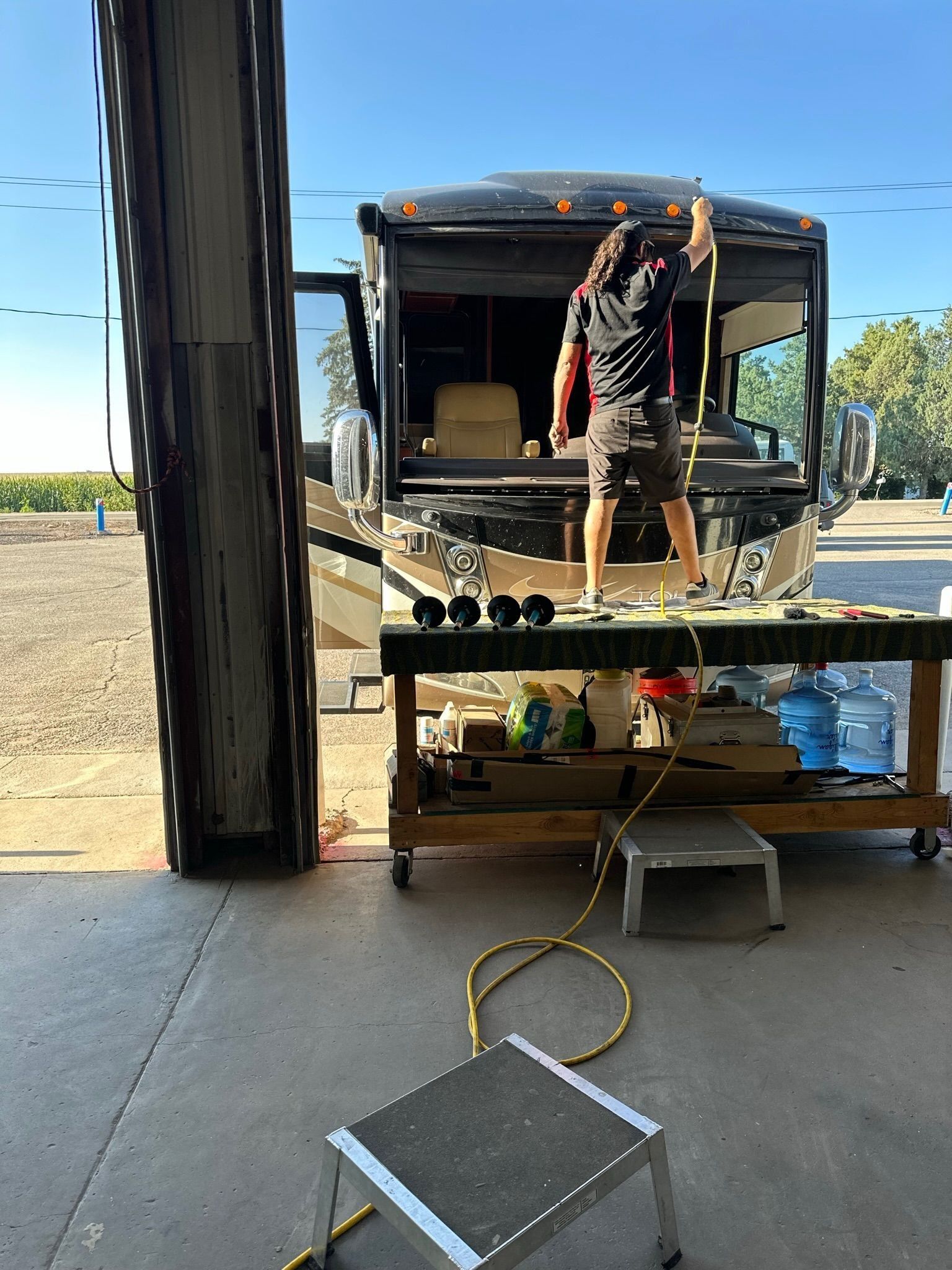 A person on a motorhome roof, working at a workbench in a garage.