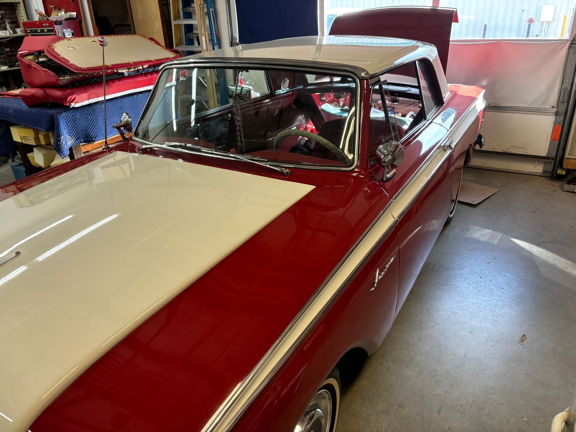 Red and white classic car with the hood open, parked inside a garage.