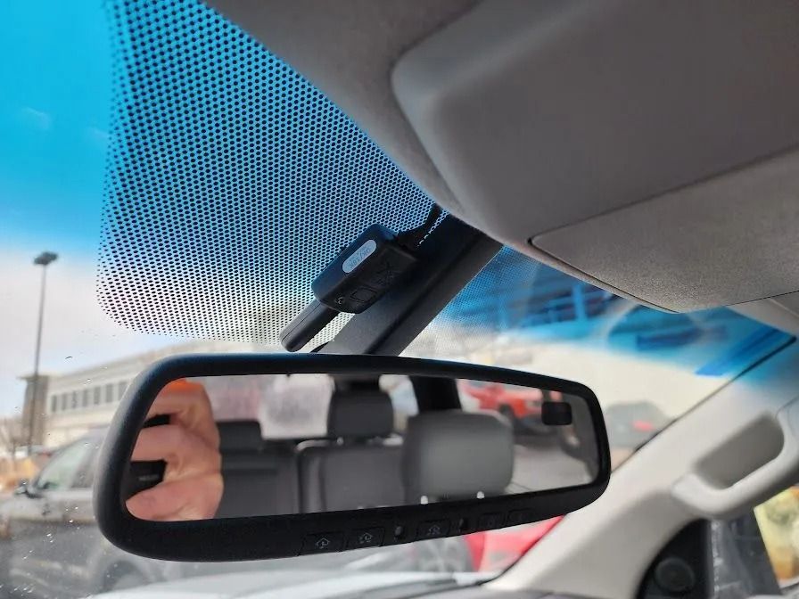 Interior view of a car: rearview mirror reflecting seats, a dashboard camera, and a windshield.