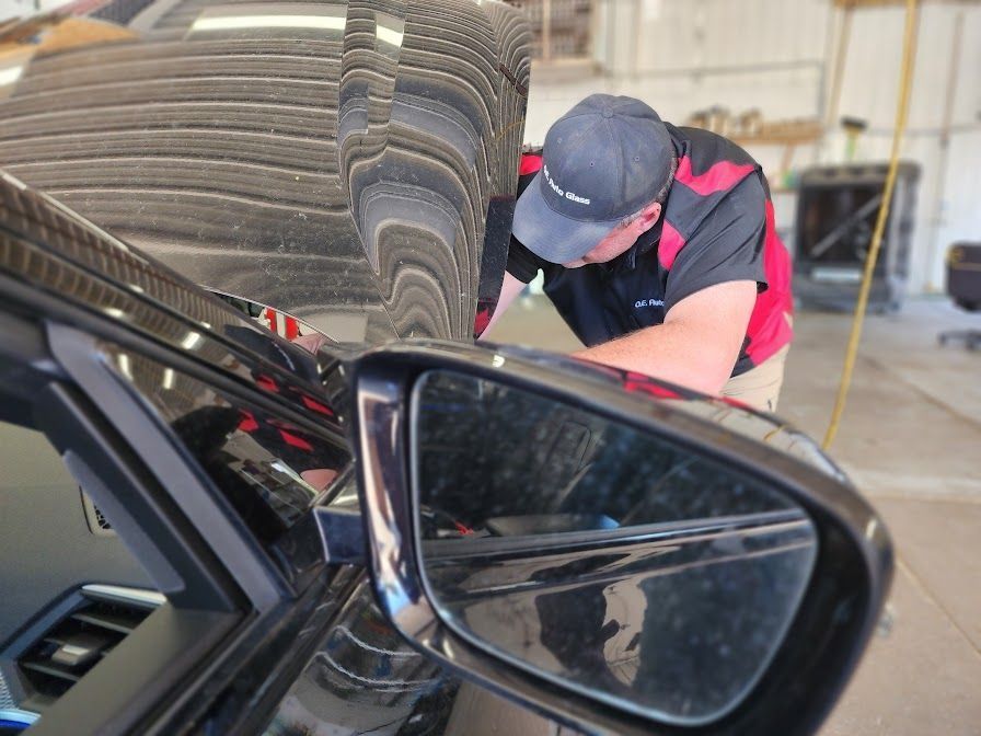 Man working on a black car near the side mirror, wearing a cap and red/black shirt, in a shop.