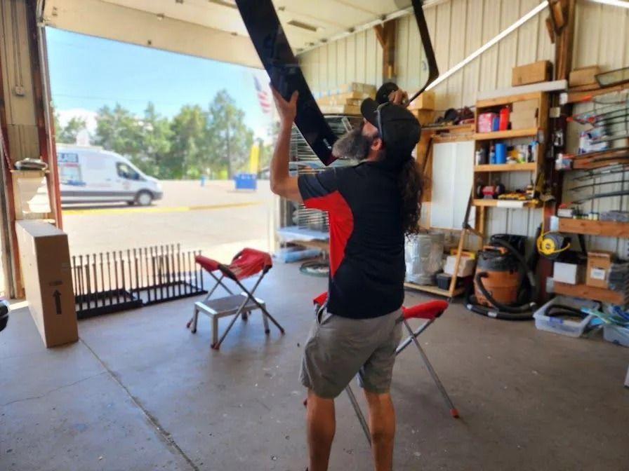 A person in a garage reaching for a black object. Open door, tools and storage.