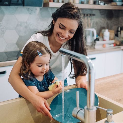 Woman helping child wash dishes at a kitchen sink