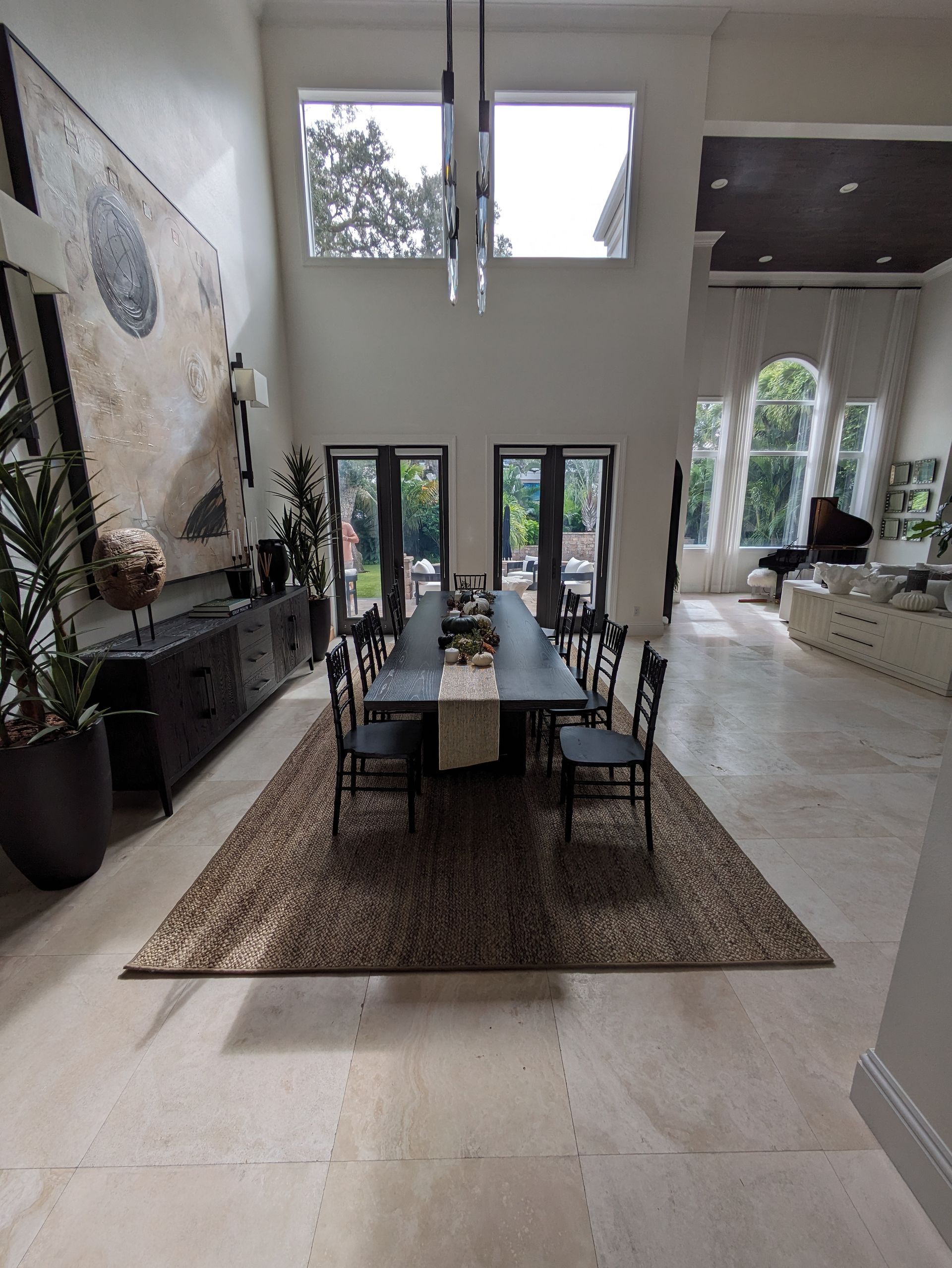 Formal dining room with long black table, rug, chairs, and artwork. High ceilings, windows.