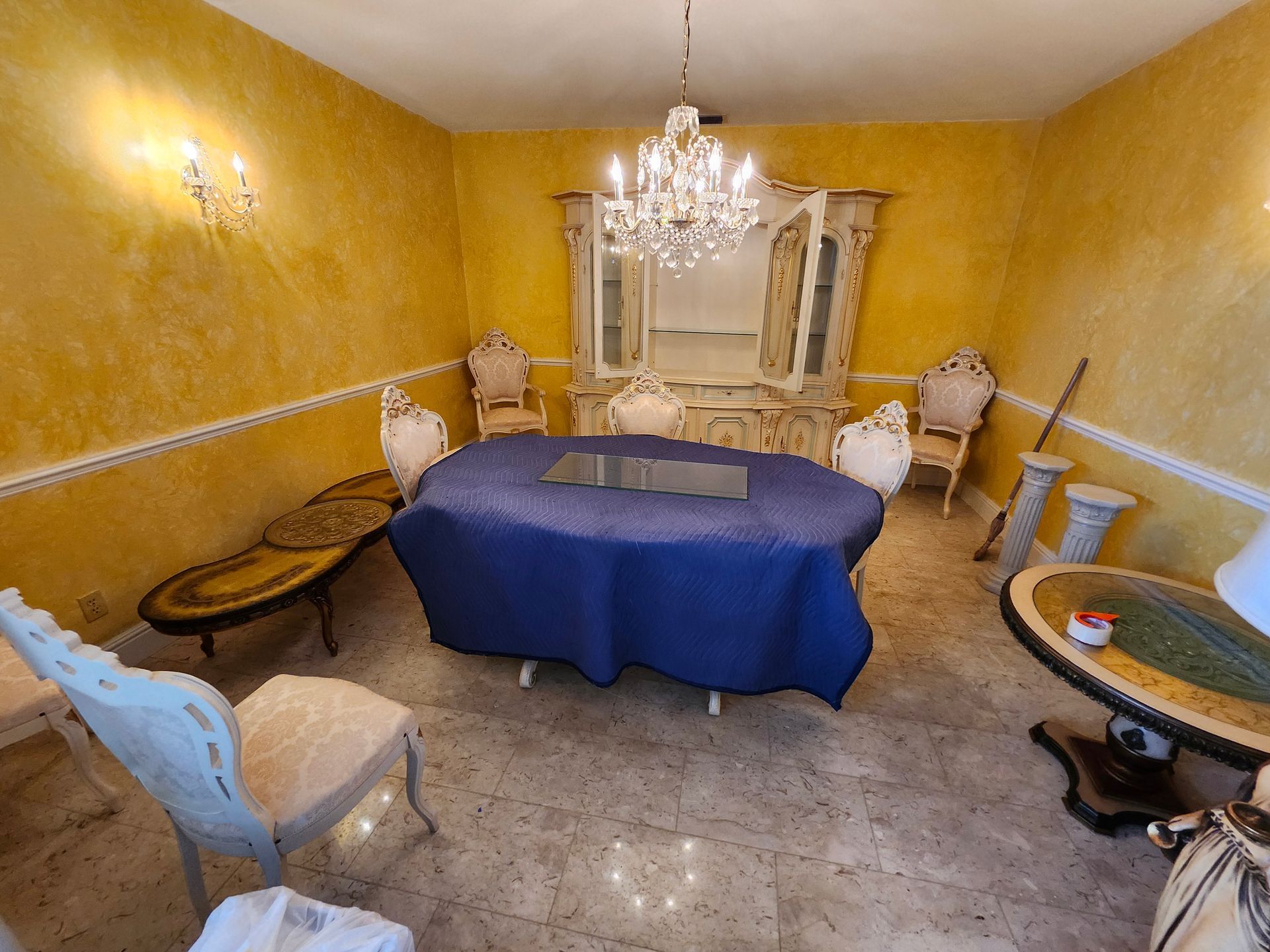 Elegant dining room with yellow walls, a blue-covered table, ornate furniture, and a chandelier.