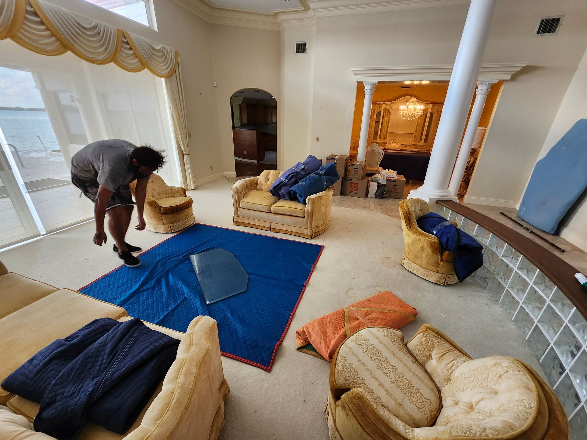 Person packing furniture in a bright room with arched doorway and large windows.