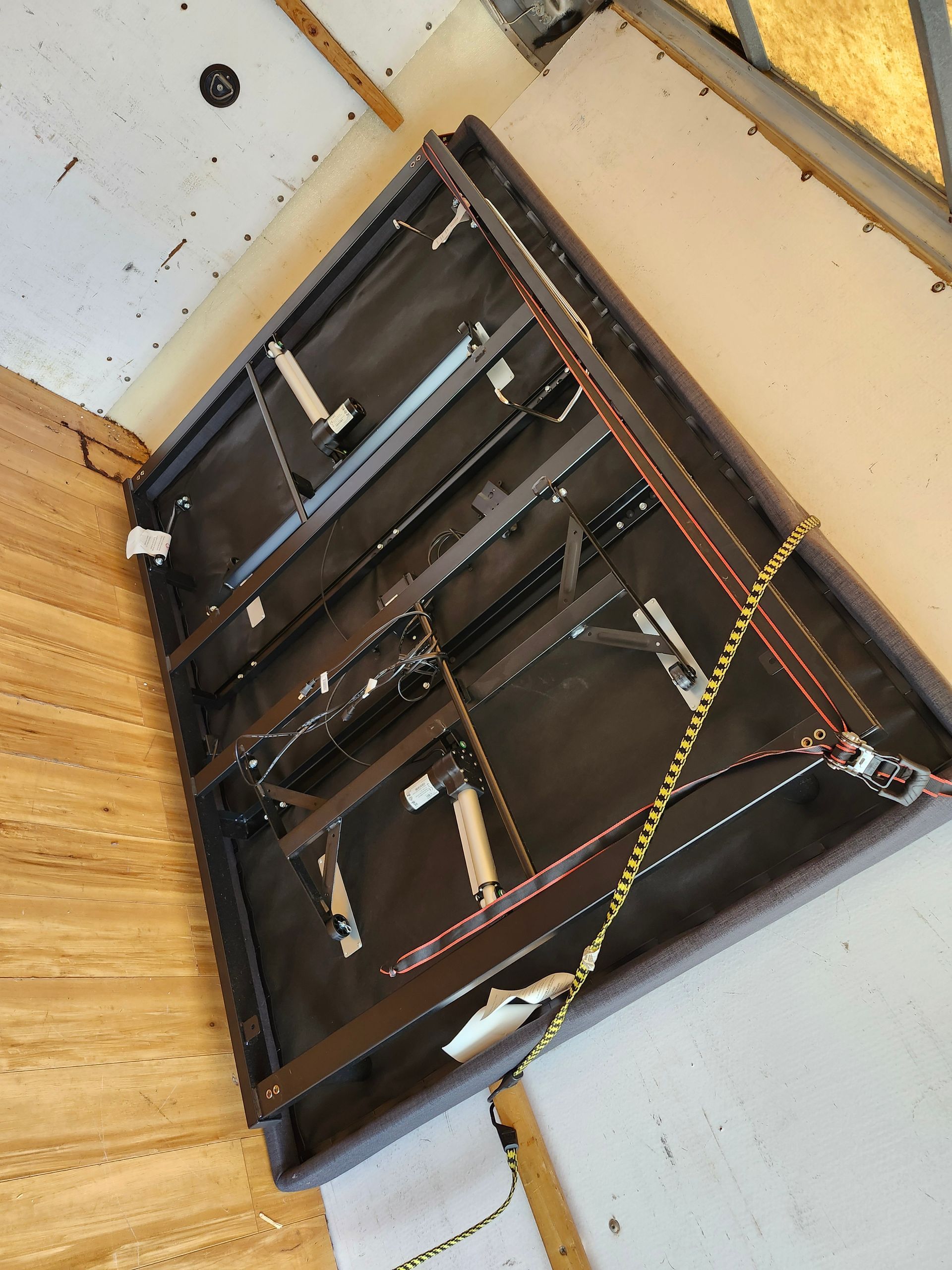 Inside view of a rectangular, dark-colored object with metal frames and wires, likely a piece of furniture or equipment.
