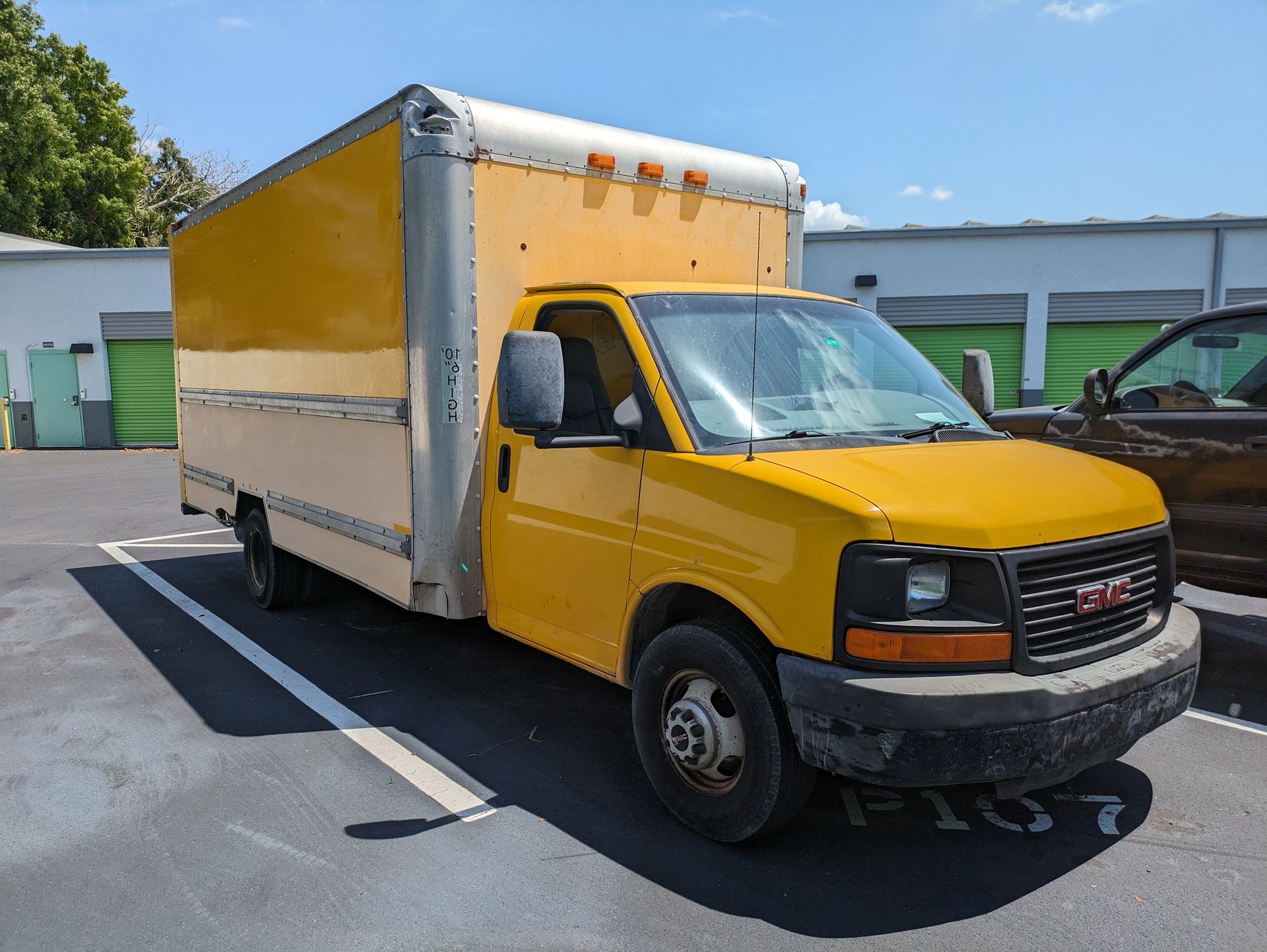 Yellow box truck parked in a lot with a storage facility in the background.