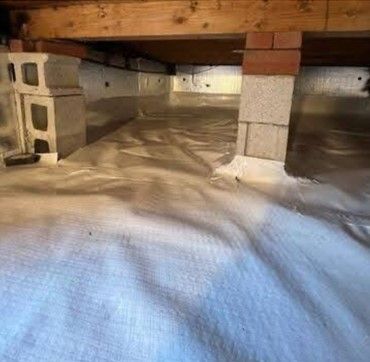 A basement with a crawl space covered in plastic and bricks.